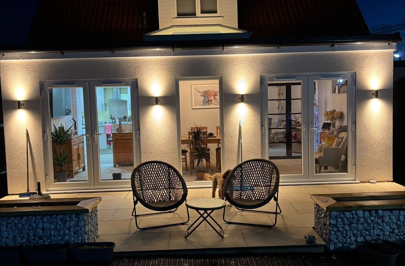 Rendered extension lit at night by up and down wall lights fitted across the patio elevation